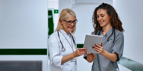 Doctors laughing and talking in a hospital hallway, showcasing positive teamwork between older and younger female doctors