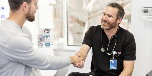 Smiling male doctor offering a handshake to a young man during a medical consultation in a professional healthcare setting.