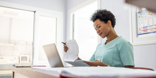 Nurse in green medical uniform filing patient paperwork in a hospital office.