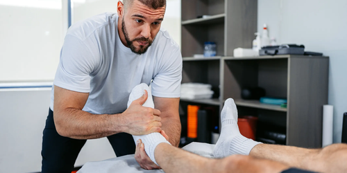Physical therapist adjusting a male client’s leg in his office, helping with rehabilitation exercises.